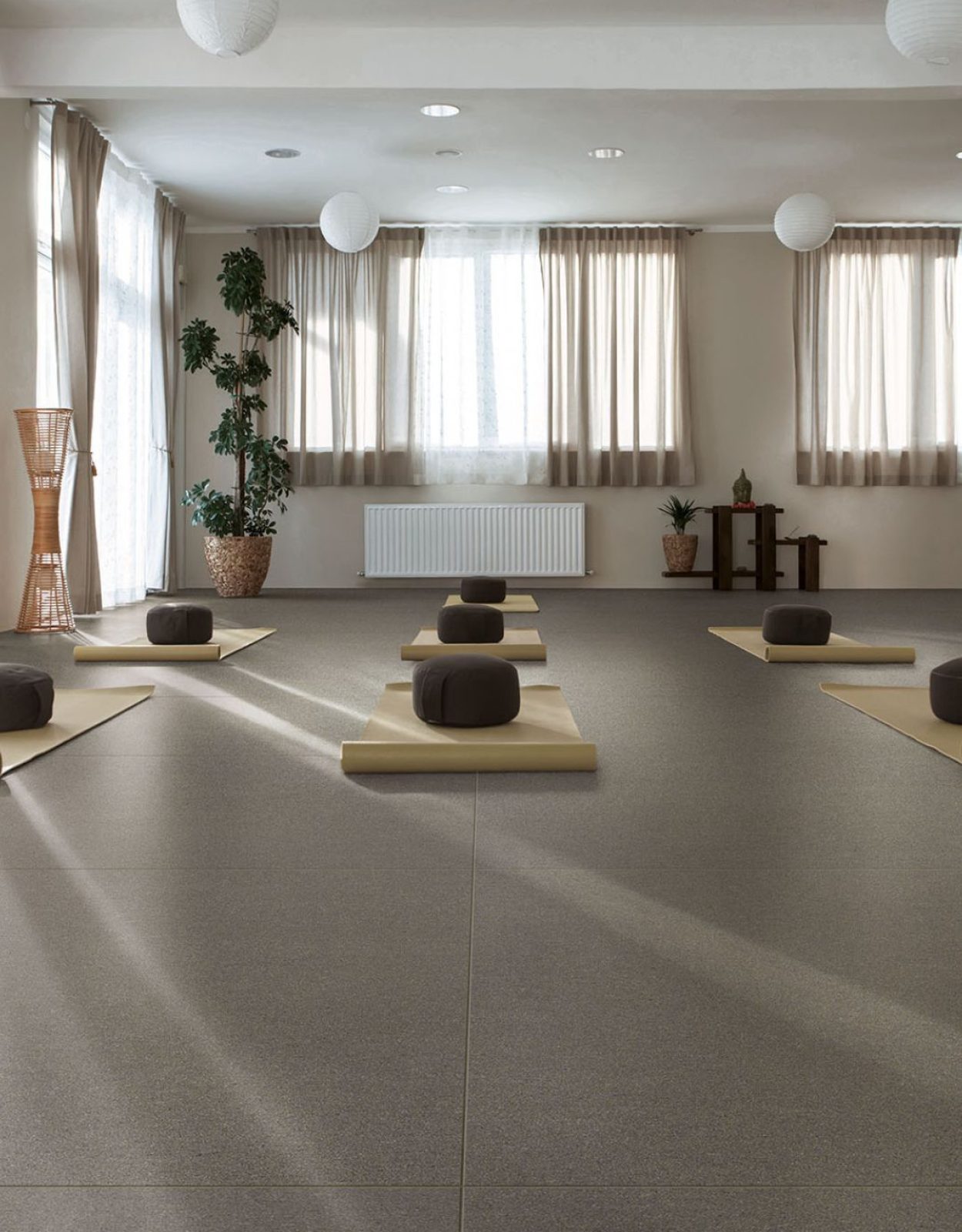 Immagine per la galleria della serie basalto. Living con pavimento realizzato con la collezione Basalto Grigio. Ci sono 2 finestre e 2 porte finestre. Sul pvimento sono appoggiati dei materassini da yoga color ocra.